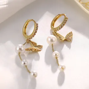 Detaillierte Nahaufnahme eleganter goldener Reifenohrringe mit Schmetterlingen und Perlen.