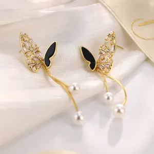 Detailaufnahme der goldenen Schmetterlings-Ohrringe mit schwarzer Emaille und weißen Perlen.