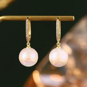 Nahaufnahme von goldenen Creolen mit funkelnden Zirkonen und irisierenden Perlen