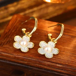 Nahaufnahme von goldenen Blumenohrringen mit Naturperle und glitzernden Blättern