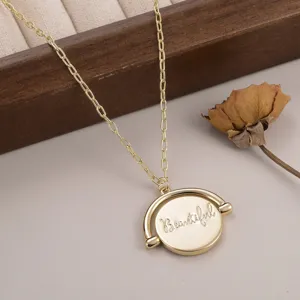 Gros plan d'un collier doré avec pendentif rotatif et gravure du mot Beautiful
