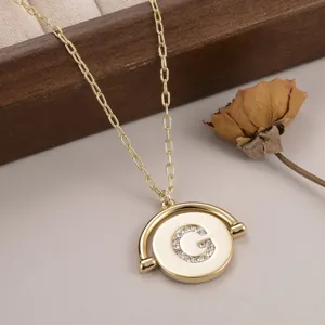 Détail en gros plan du collier à pendentif rond doré avec lettre G en cristal