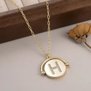 Gros plan d'un pendentif circulaire doré rotatif orné d'une lettre H en strass