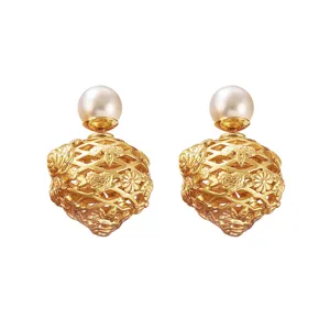 Gros plan détaillé de boucles d'oreilles cage à roses évidées dorées avec perle blanche.
