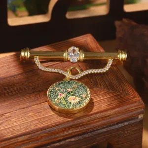 Close-up of vintage gold-toned brooch featuring crystal and green enamel floral pendant