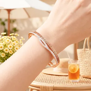Dettaglio ravvicinato di un bracciale in oro rosa con motivo greco e strass al polso