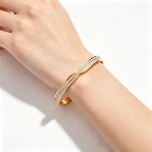 Detailopname van een gouden roestvrijstalen armband met schelpinleg en kristallen om de pols