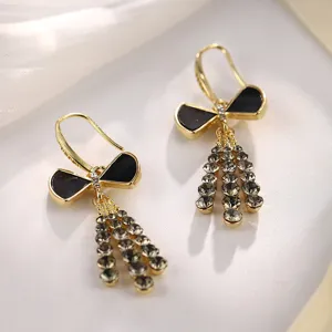Elegante goldene Schleifenohrringe mit schwarzer Emaille und funkelnden Quastenanhängern