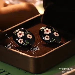 Close-up of black oval enamel earrings with white flower and green leaf patterns.