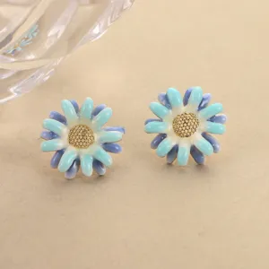 Detail of gradient blue enamel flower stud earrings with golden center on beige background