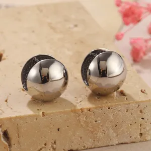 Primo piano di orecchini a sfera in metallo argento lucido su una base di pietra grezza.