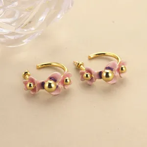 Close-up detail of enamel flower hoop earrings with pink petals and gold accents.