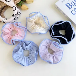 Top view of five colorful fabric scrunchies with blue striped trim on a white surface