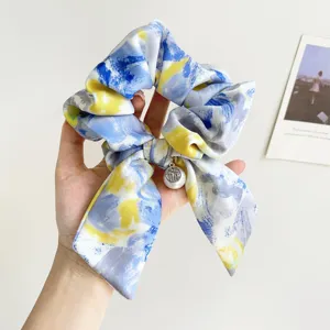 Close-up of an oil painting style blue and yellow gradient scrunchie with a pearl charm.