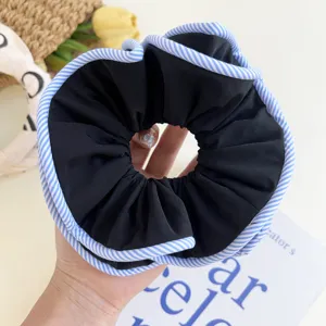 Detailed close-up of a large black fabric scrunchie with blue and white striped edges