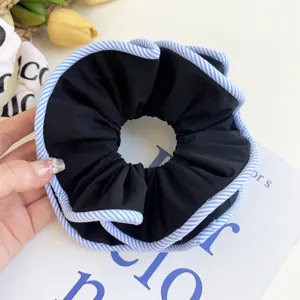 Close-up of large black fabric scrunchie with blue and white striped edges