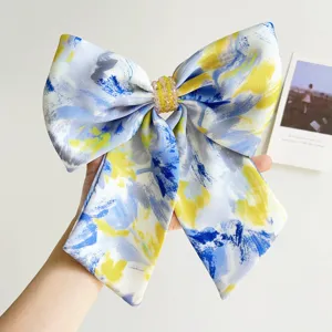Detailed view of a large oil painting style hair bow with yellow beads held by hand.