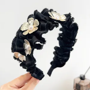 Gedetailleerde weergave van een zwarte geplooide haarband met gouden bloemen en parels.