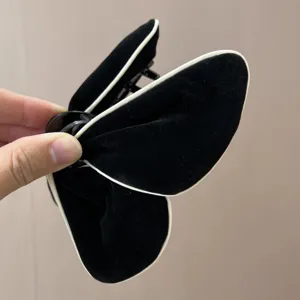 Détail d'une pince à cheveux papillon en velours noir avec un liseré blanc élégant.