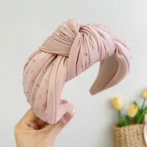 Detailweergave van een roze geknoopte stoffen haarband met glanzende strass-steentjes.