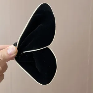Détail montrant la texture de la pince papillon en velours noir avec bordure blanche.