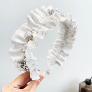 Detailopname van een witte gerimpelde haarband met parels en bloemdetails