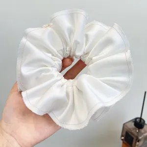 Close-up van een grote witte geplooide satijnen scrunchie met delicate golvende randen.