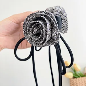 Dettaglio di un fermaglio per capelli con rosa in tessuto scozzese e lunghi nastri neri, chic.