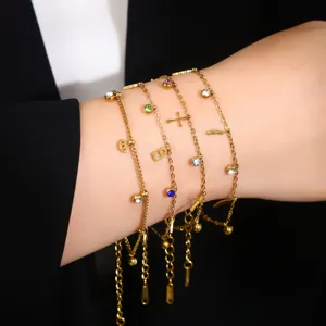 Nahaufnahme von vergoldeten Edelstahl-Charm-Armbändern mit bunten Strasssteinen am Handgelenk.