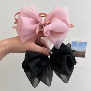 Primer plano de grandes pinzas para el cabello con lazo de malla rosa y negro en la mano.