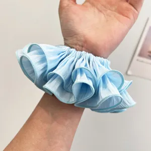 Detailansicht eines hellblauen plissierten übergroßen Scrunchie-Haargummis am Handgelenk.