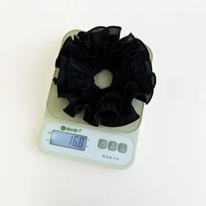Detail einer schwarzen, plissierten Oversize-Scrunchie, gewogen mit 16,8g auf Waage.