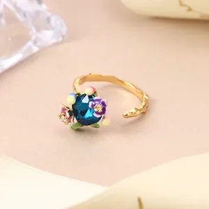 Macro view of vintage style enamel floral ring featuring a blue crystal on gold band