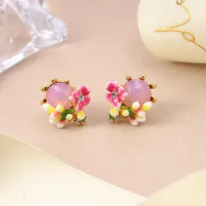 Close-up detail of floral enamel earrings with pink crystal and elegant gold-plated finish