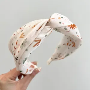 Detail view of a cream wide headband with autumn floral and leaf patterns in soft satin.