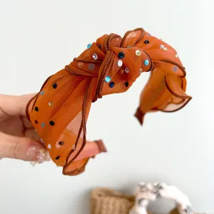 Detail van een oranje mesh geknoopte haarband met kleurrijke glimmende strassteentjes.