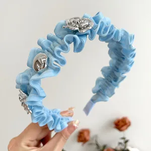 Detailansicht eines hellblauen Rüschenstirnbandes mit silbernen Rosenornamenten.