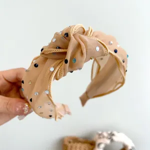 Gedetailleerde weergave van een beige geknoopte mesh hoofdband met kleurrijke stras