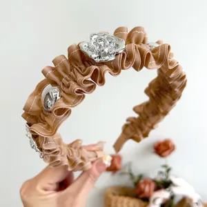 Detailansicht eines plissierten braunen Haarreifens mit einer silbernen Metallrose.