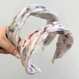 Close-up of wide-edged cross-knotted headbands with artistic watercolor floral patterns.