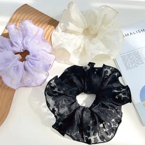 Close-up view of three elegant lace hair scrunchies in purple, white, and black colors