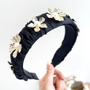 Close-up of elegant pleated black headband with golden metal flowers and pearls