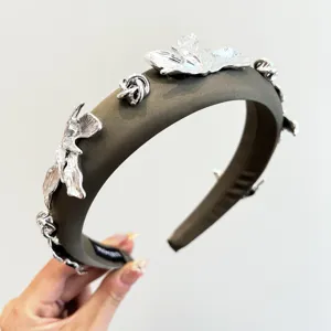 Détail rapproché des pétales métalliques argentés sur un serre-tête en tissu olive.