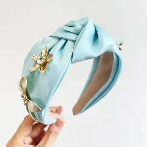 Gros plan d'un serre-tête en satin bleu clair orné de fleurs en métal doré et de cristaux.