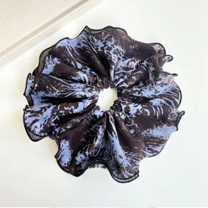 Close-up view of a blue and brown tie-dye fabric scrunchie featuring elegant ruffled edges
