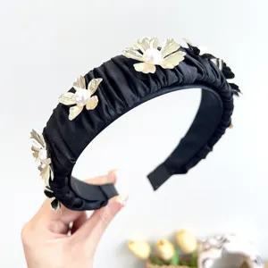 Detailed close-up of a black ruched headband with gold metal flowers and pearls.