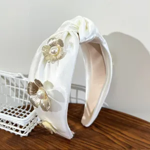 Close-up of white satin knotted headband with golden metal flowers and pearls