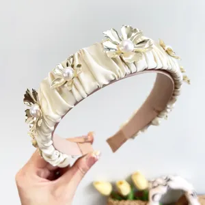 Macro detail of pleated cream headband featuring metallic gold flowers and pearls