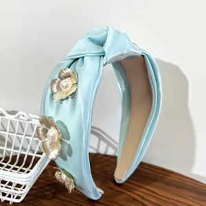 Macro view of light blue satin knotted headband with gold metallic flowers and pearls