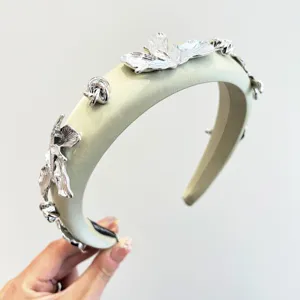 Gros plan d'un serre-tête en satin vert sauge avec des détails de pétales de fleurs en argent.